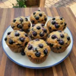 Bakery style blueberry muffins on a white ceramic dessert plate with a blue rim