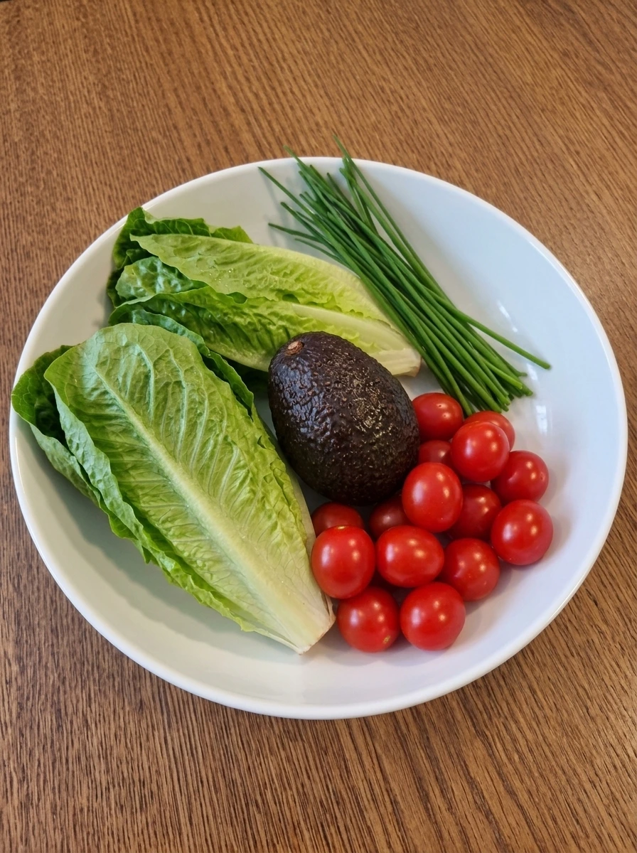 Washed romaine, tomatoes, avocado, and chives in a white serving bowl