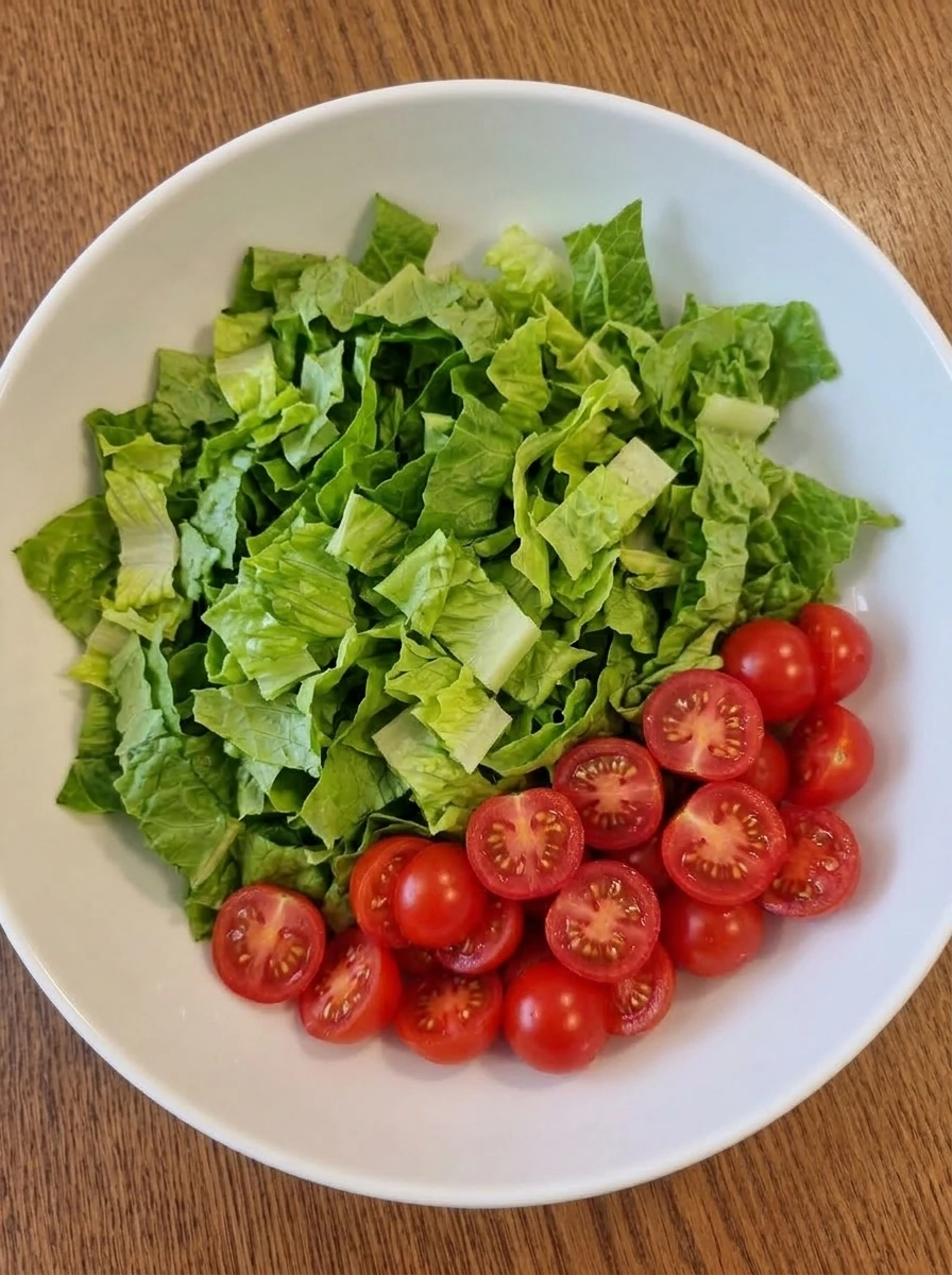 Chopped romaine and halved tomatoes in a white serving bowl