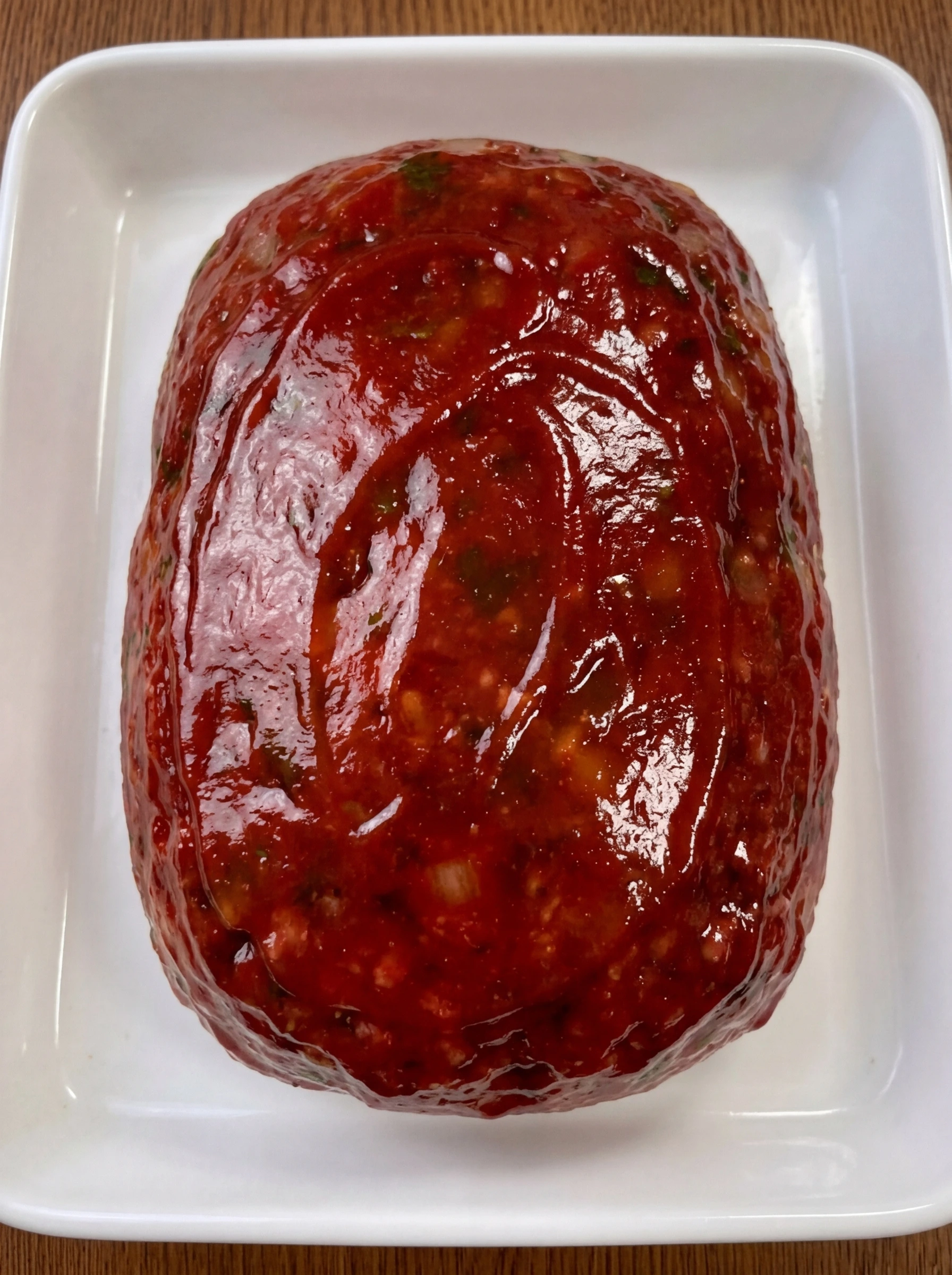 Raw glazed meatloaf on a white ceramic tray