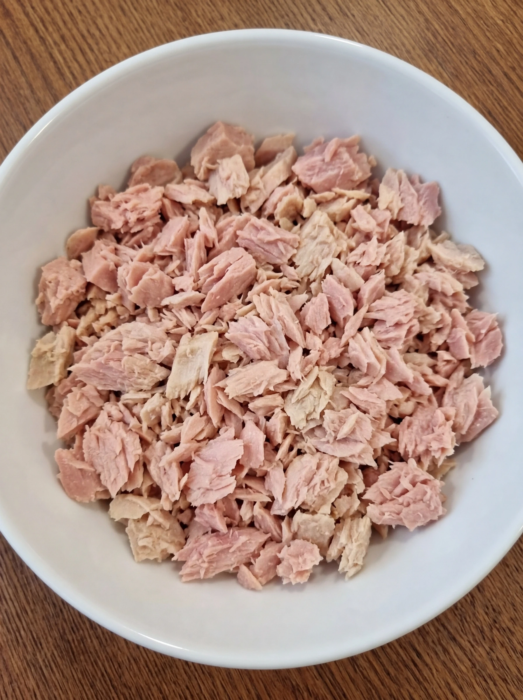 Drained flaked tuna in a white ceramic bowl