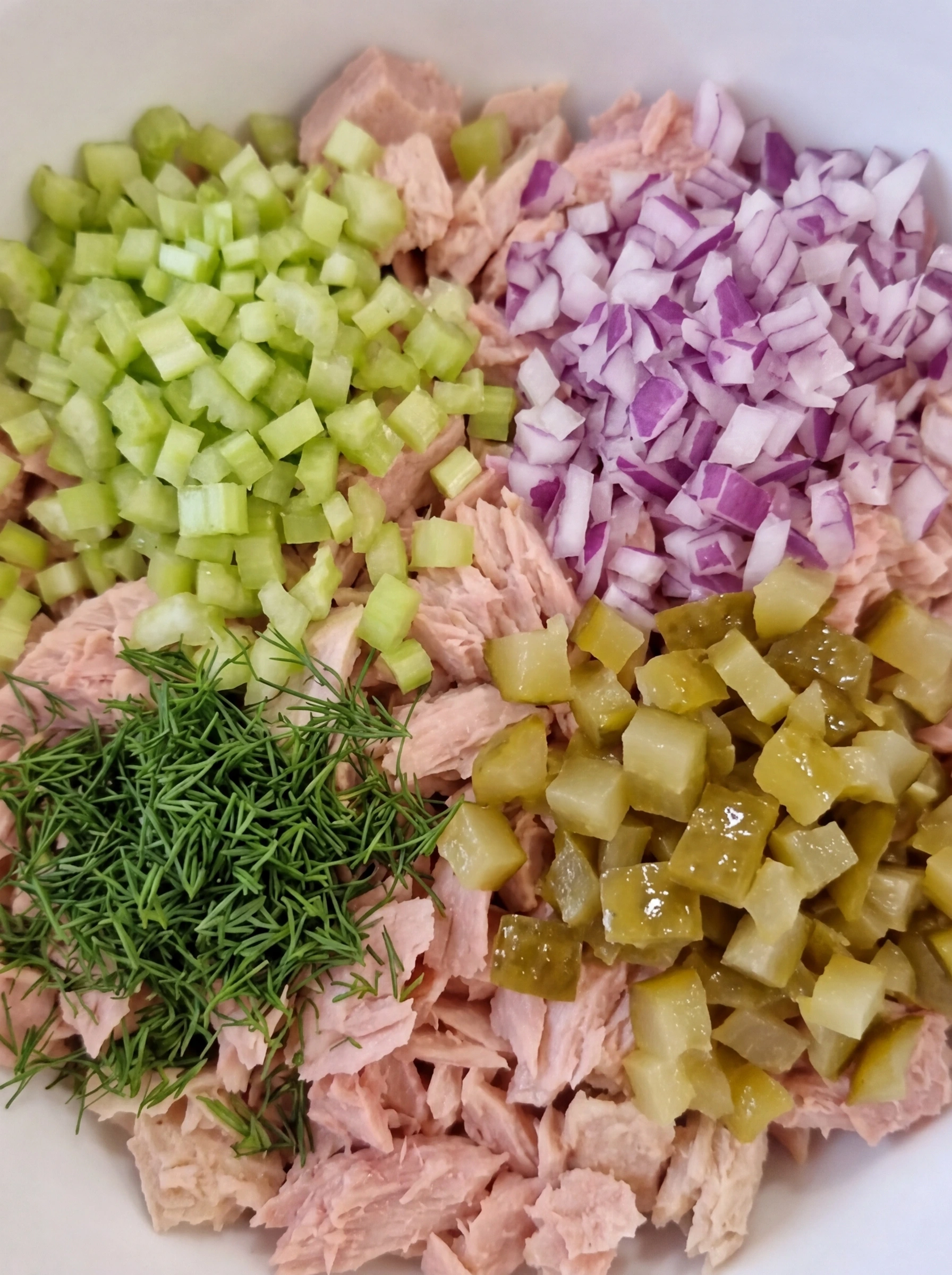 Flaked tuna with chopped celery onion pickles and dill in a white ceramic bowl