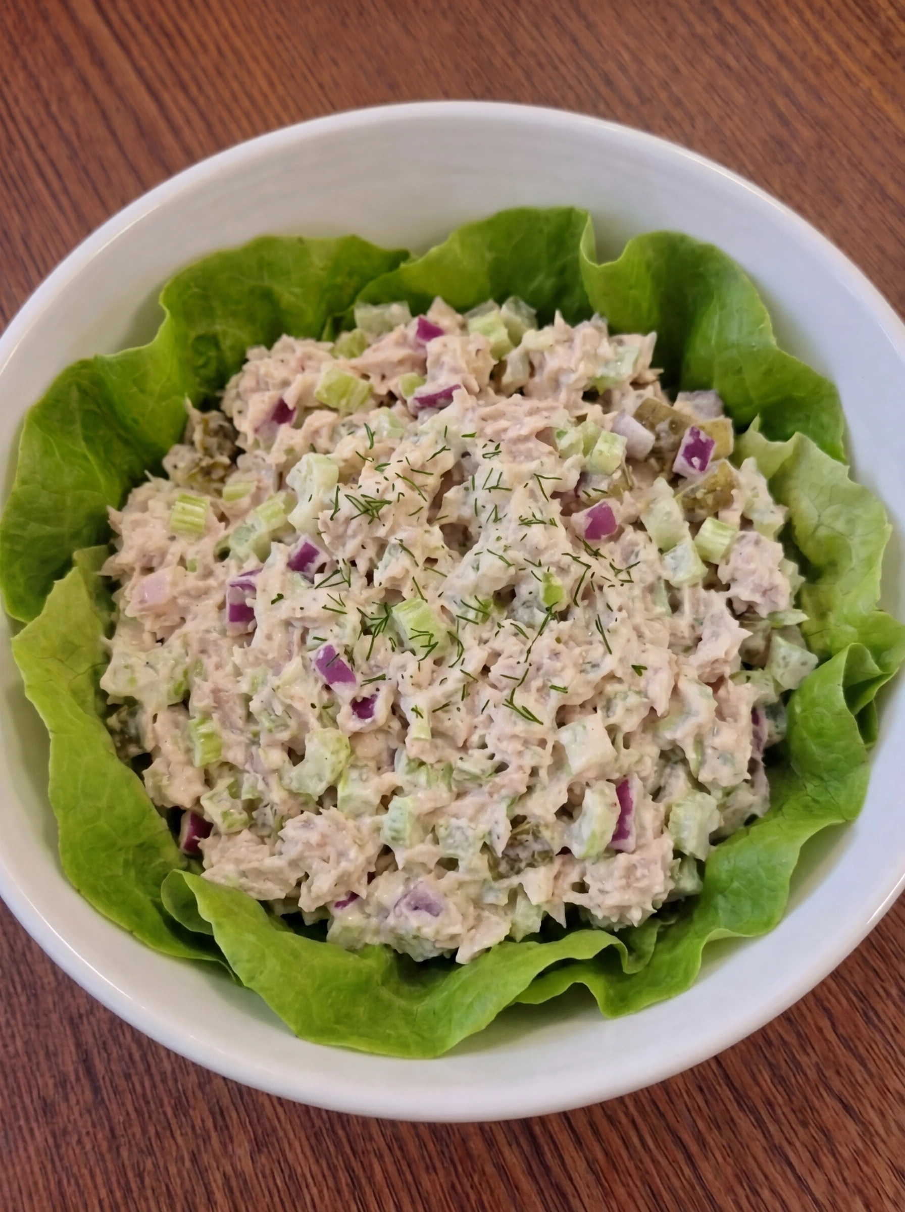 Finished creamy tuna salad garnished and ready to serve in a white ceramic bowl