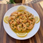 Garlic butter shrimp served with lemon and parsley on a white oval ceramic plate