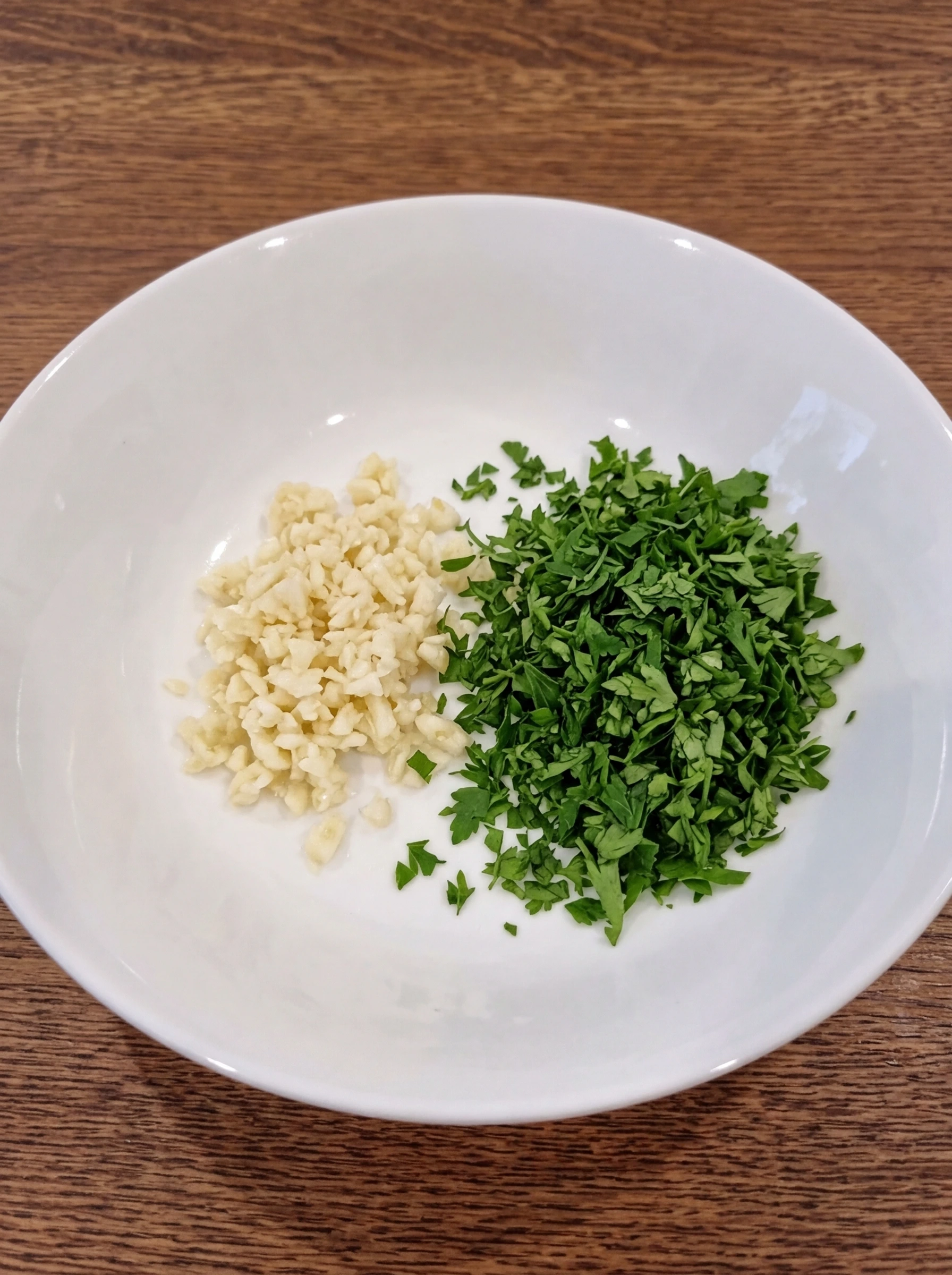 Minced garlic and chopped parsley in a white ceramic pasta bowl