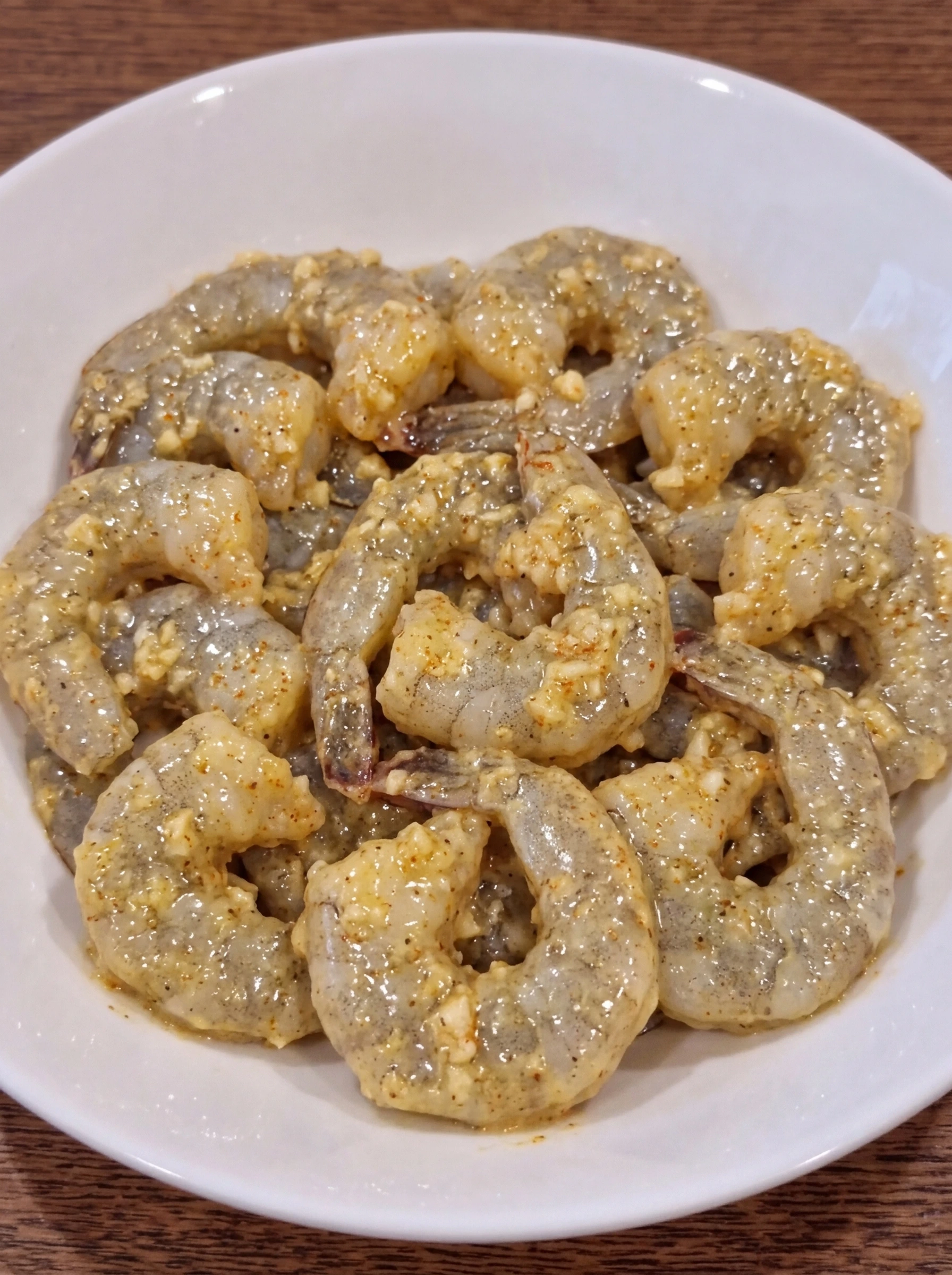 Raw shrimp coated in garlic butter mixture in a white ceramic pasta bowl