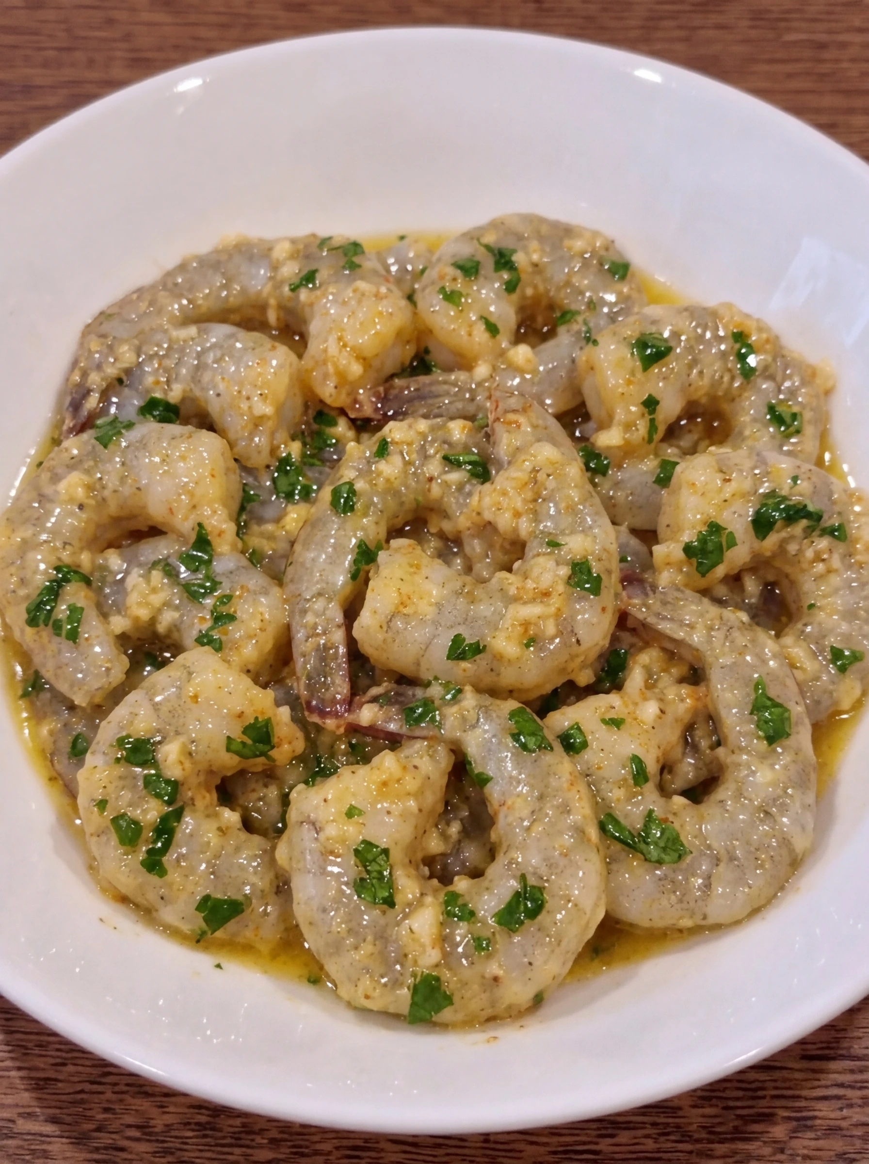 Raw shrimp resting in garlic butter lemon mixture in a white ceramic pasta bowl