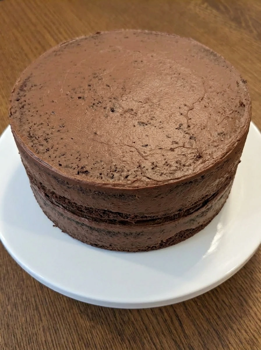 Two layer chocolate cake with crumb coat on a white ceramic cake stand
