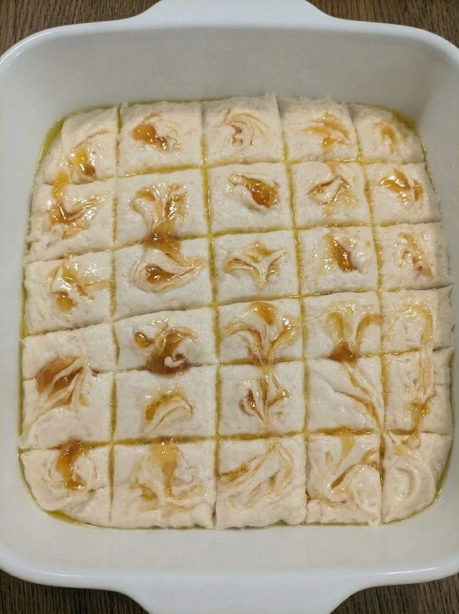 Peach preserves swirled across biscuit dough in a white ceramic baking dish