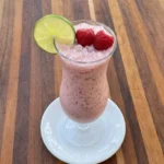 Finished Raspberry Colada in a clear hurricane glass with raspberries and lime