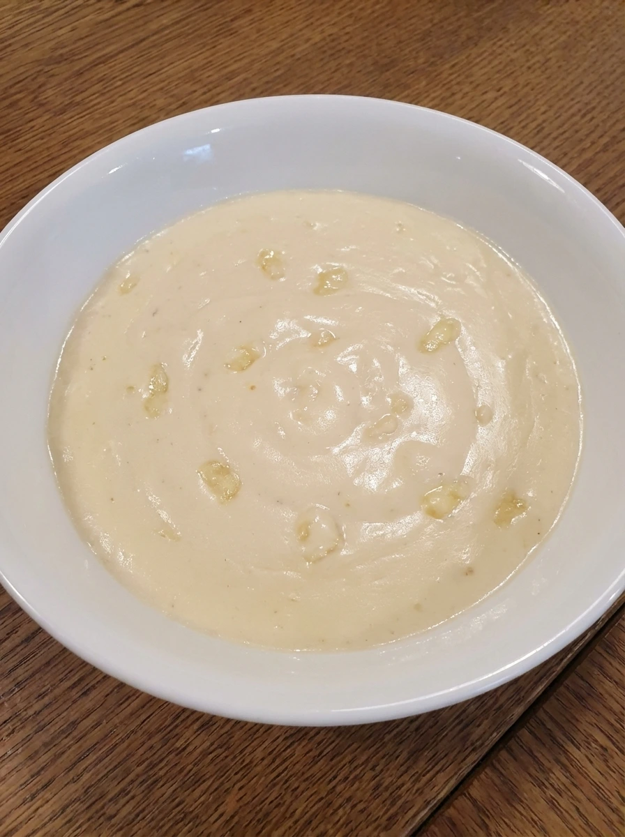 Pale creamy Alfredo sauce with melted parmesan in a white bowl