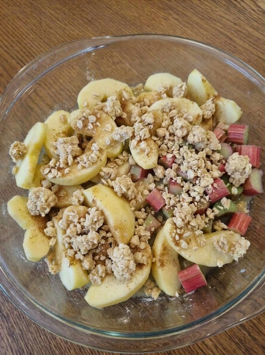 Crumble topping scattered over apple rhubarb filling.