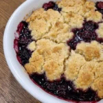Blackberry Cobbler with bubbling berries and golden uneven topping in a rustic round white stoneware plate