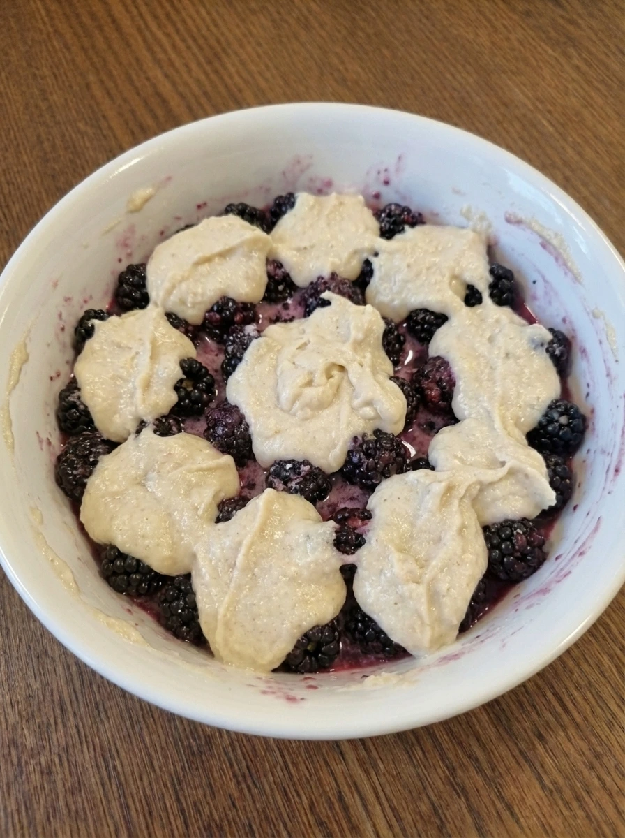 Blackberries layered with spoonfuls of batter in a white baking dish