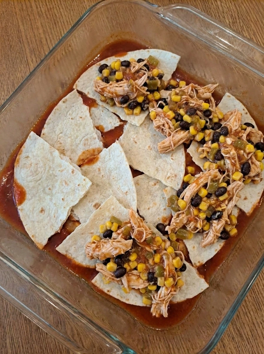 Tortillas and chicken filling layered in a baking dish for enchilada casserole