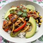 Chicken Fajita Bowl with rice browned chicken peppers onions beans corn avocado salsa and cilantro in a white bowl