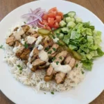 Chicken Shawarma Plate with browned chicken rice salad garlic sauce and pickles on a white plate