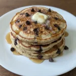Chocolate Chip Pancakes stacked on a white ceramic plate with melted chocolate and maple syrup