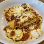 Classic Beef Lasagna on an oval white ceramic plate with melted cheese and browned edges