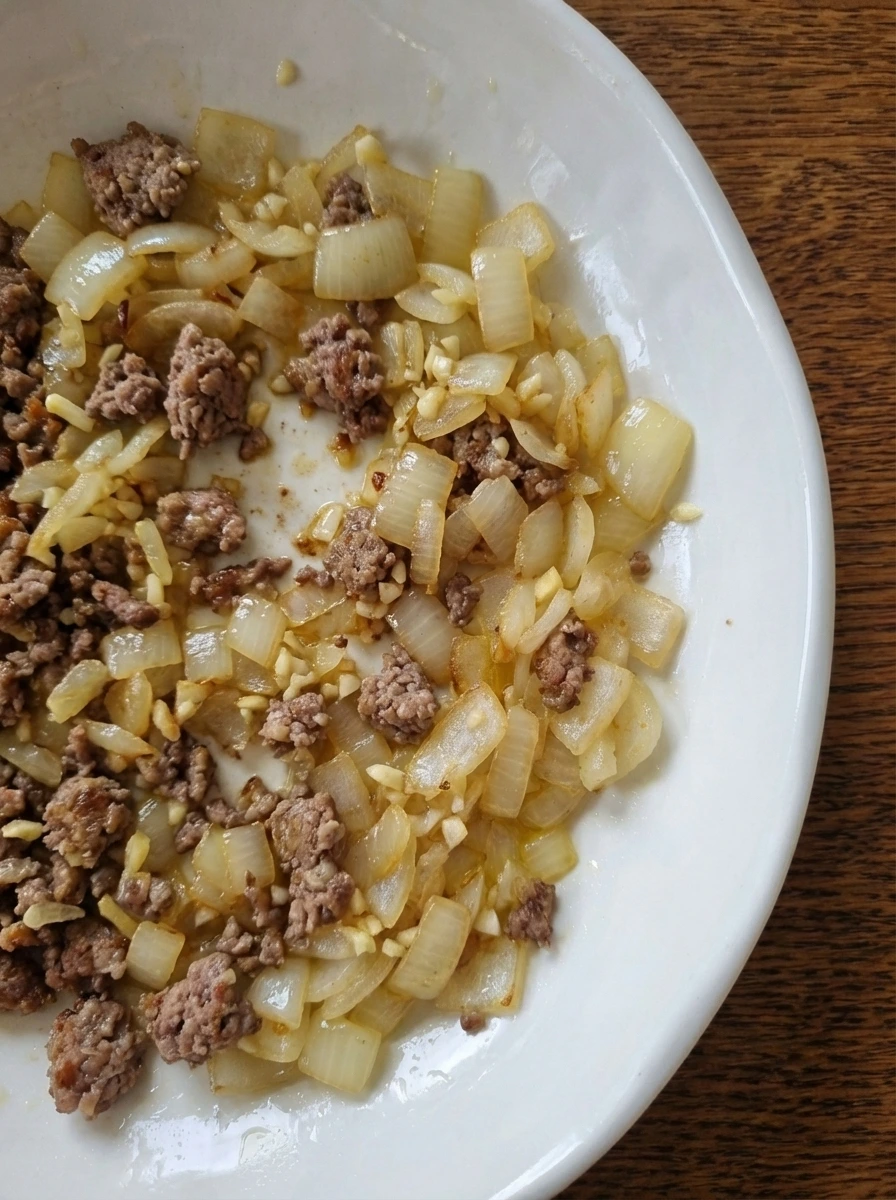 Browned beef mixed with onion and garlic in a natural white dish