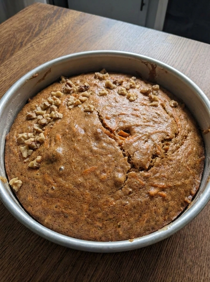 Freshly baked carrot cake with a domed golden top in a cake pan.