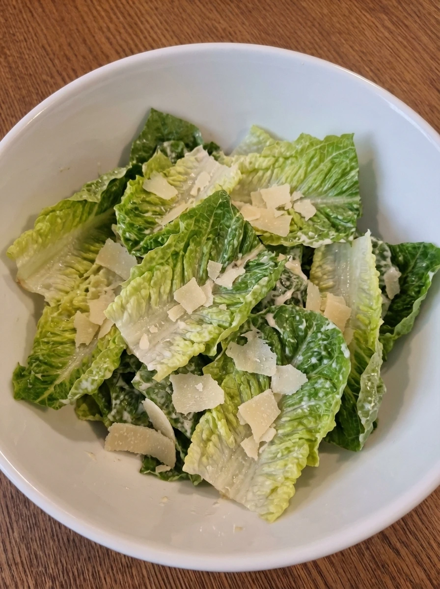 Romaine tossed with Caesar dressing and Parmesan in a white bowl