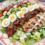 Classic Cobb Salad on a white oval platter with chicken bacon eggs avocado tomatoes and blue cheese