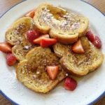 Classic French Toast on a white blue rim plate with golden brown slices syrup and strawberries
