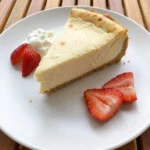 Classic New York Cheesecake slice on a white ceramic dessert plate with strawberries and whipped cream
