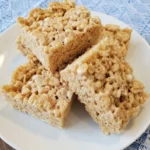 Classic Rice Krispie Treats stacked in a white plate with gooey marshmallow texture and uneven homemade edges