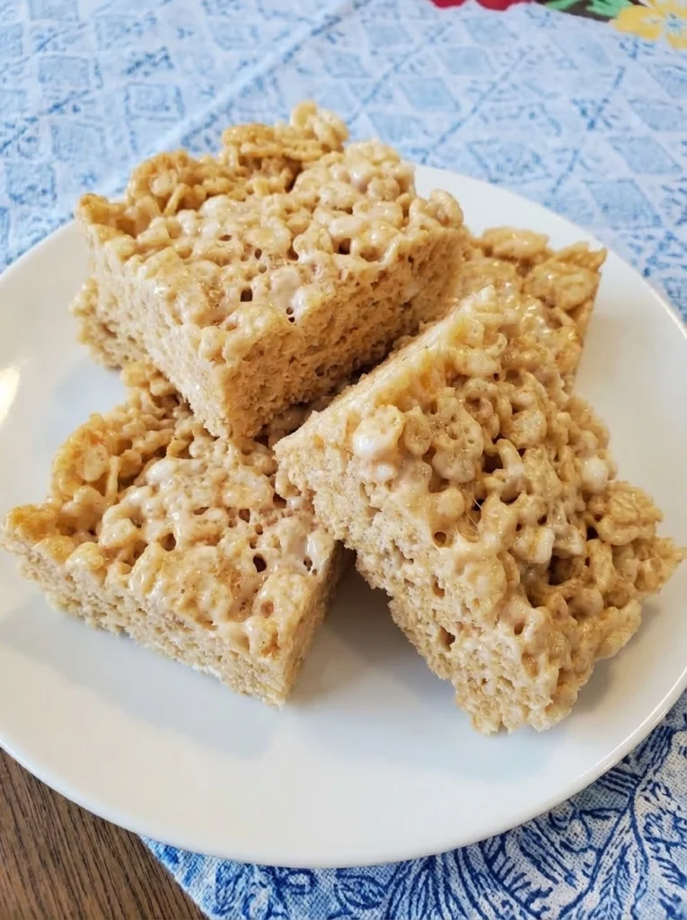 Classic Rice Krispie Treats stacked in a white plate with gooey marshmallow texture and uneven homemade edges