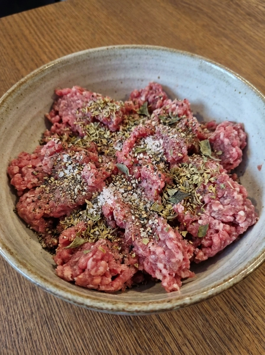 Raw ground beef seasoned with herbs salt and pepper in a bowl