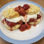 Classic Strawberry Shortcake with golden biscuits syrupy strawberries and whipped cream on a white stoneware plate