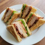 Classic Turkey Club Sandwich on a white plate with toasted bread turkey bacon lettuce tomato and mayo.