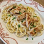 Creamy Chicken Alfredo Pasta on a rustic white ceramic dinner plate with sliced chicken and uneven parmesan sauce