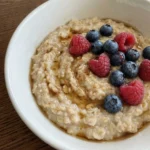 Creamy Old Fashioned Oatmeal in a rustic white shallow ceramic bowl with maple syrup and berries