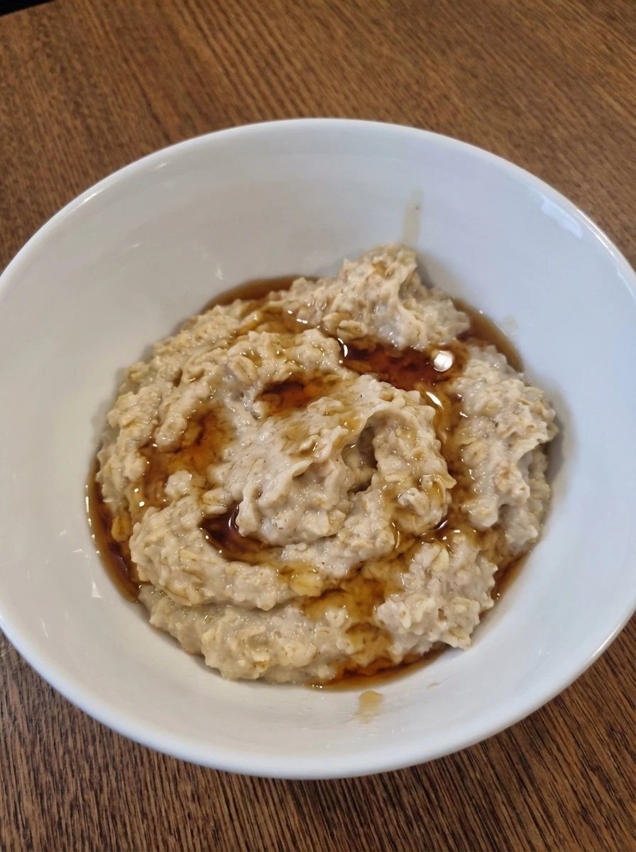 Creamy oatmeal spooned into a natural white dish with maple syrup drizzled on top