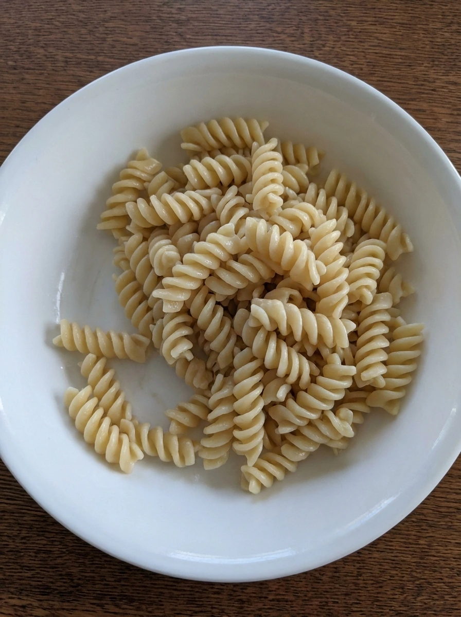 Cooked rotini pasta cooled in a white ceramic bowl.