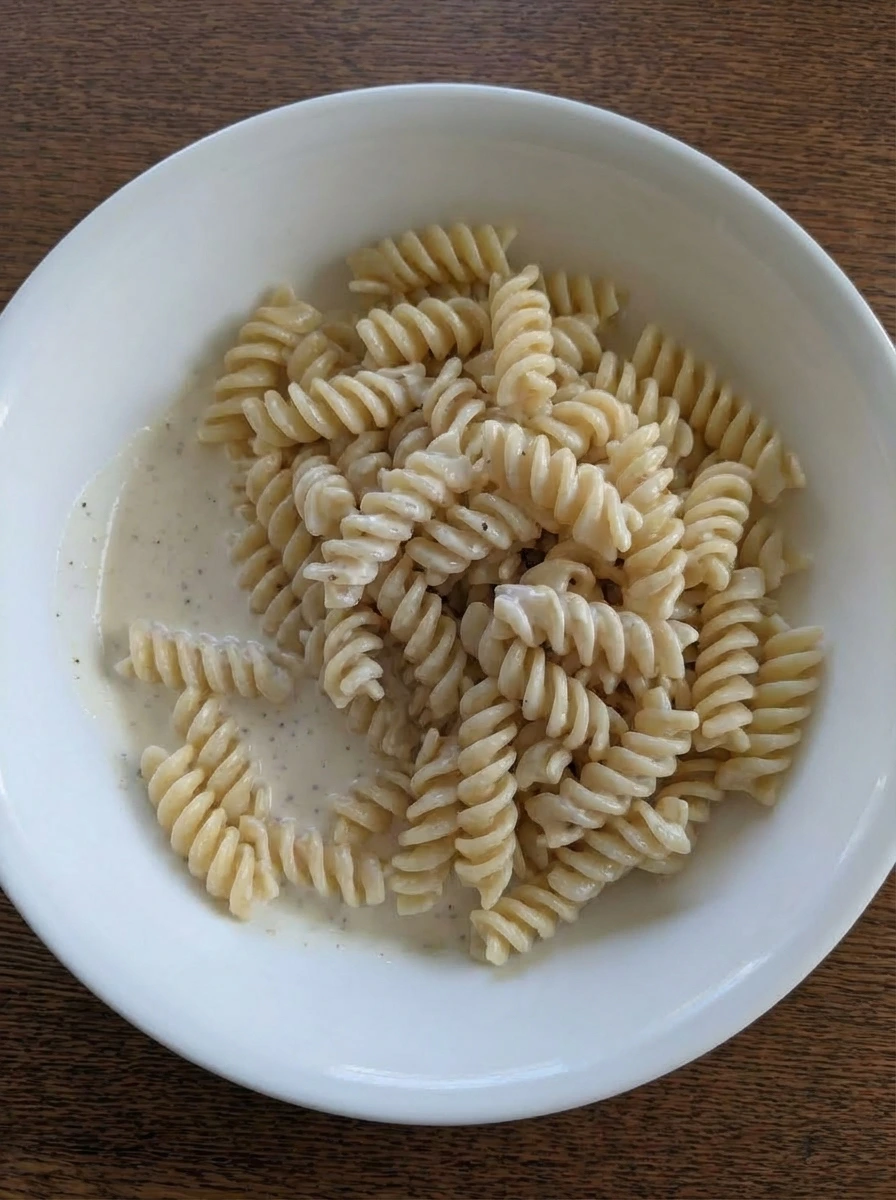 Rotini being coated with creamy dressing in a white ceramic bowl.