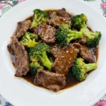 Crock Pot Beef and Broccoli served on a white plate with glossy sauce and sesame seeds