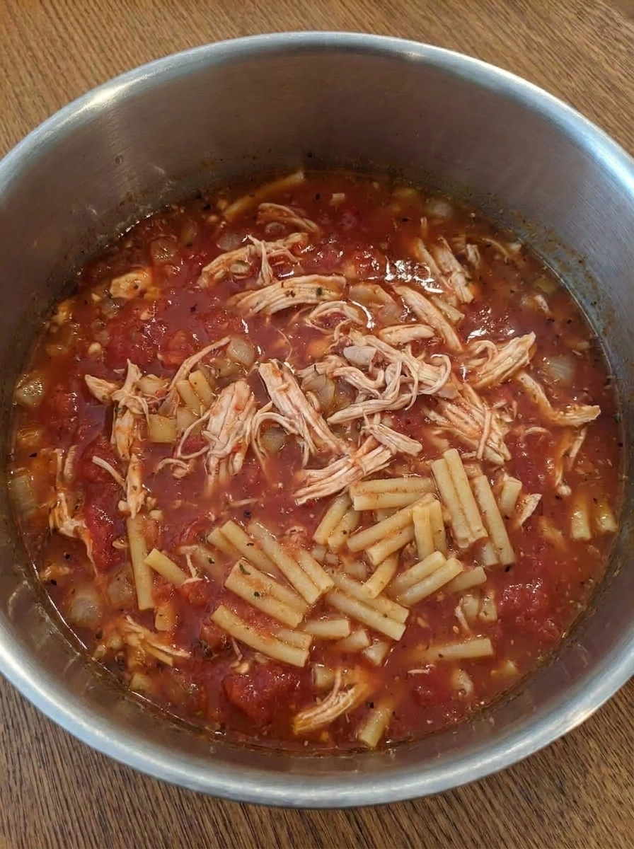 Shredded chicken and pasta simmering in tomato broth.