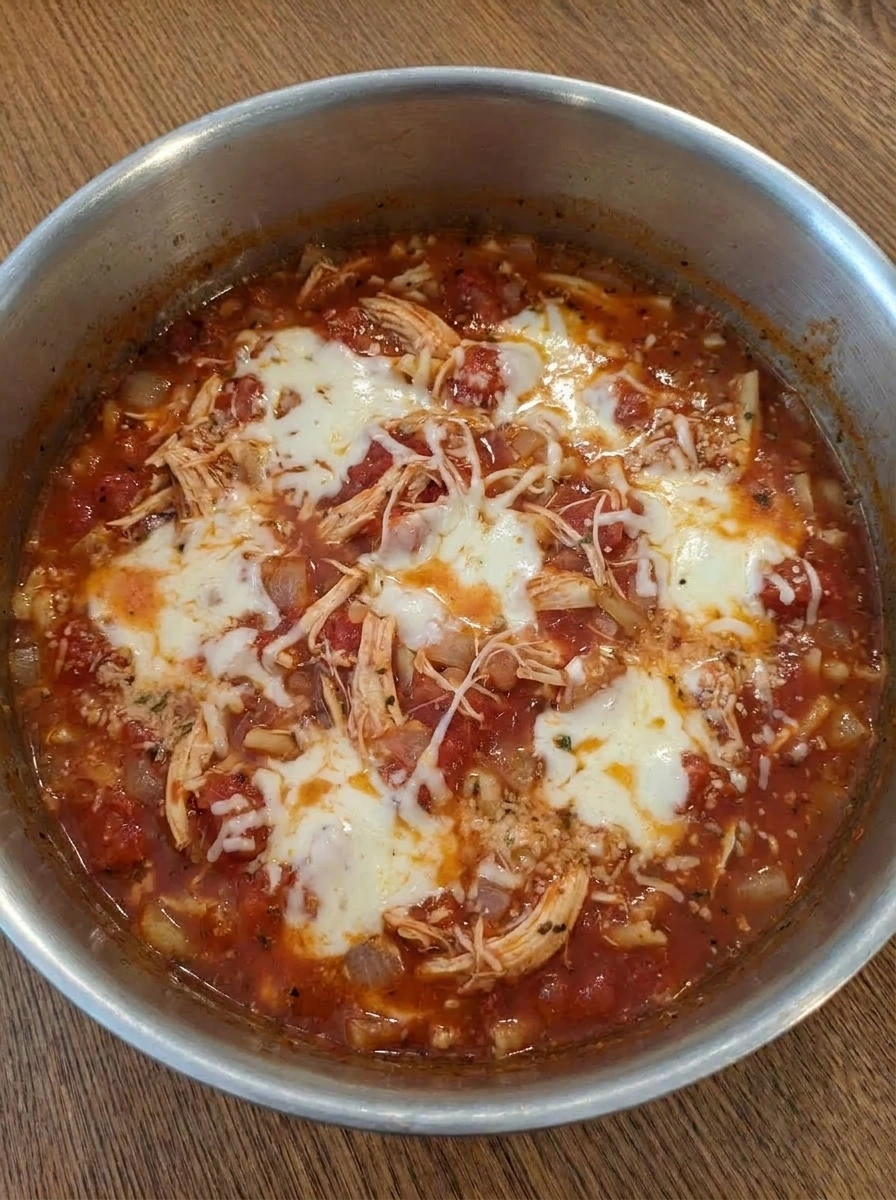 Cheese melting into chicken parmesan soup with shredded chicken and pasta.
