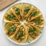 Crockpot Cilantro Lime Chicken served in yellow corn tortillas with cilantro and salsa verde.