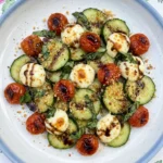 Cucumber Caprese Salad on a white ceramic plate with warm mozzarella and blistered tomatoes