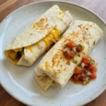 Easy Breakfast Burritos on a rustic round ceramic plate with melted cheese and golden browned tortillas