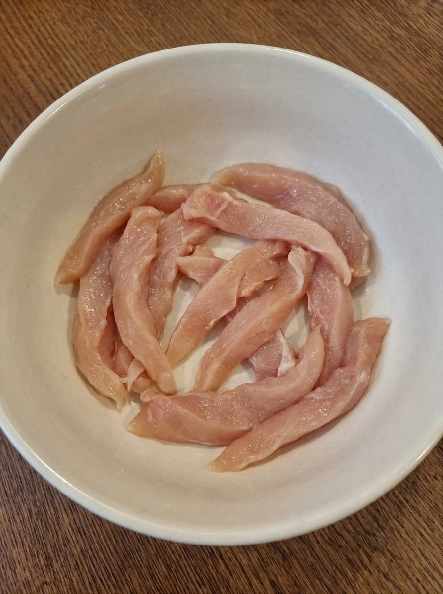 Thin raw chicken strips in a ceramic bowl