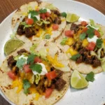 Easy Ground Beef Tacos plated with seasoned beef softened cheese lettuce tomatoes sour cream and cilantro