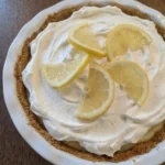 Easy Lemon Cream Pie on a rustic white ceramic pie plate with whipped cream and lemon slices
