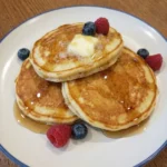 Fluffy Buttermilk Pancakes stacked on a white stoneware plate with melting butter and maple syrup