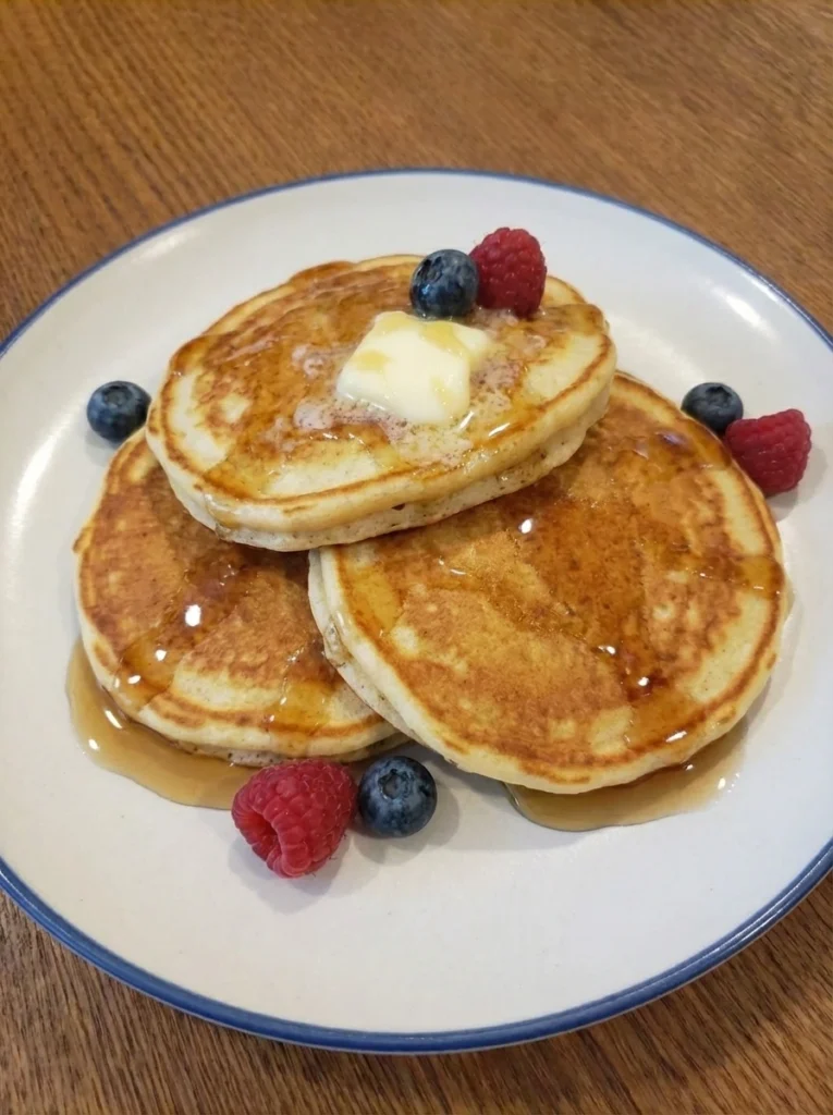 Fluffy Buttermilk Pancakes stacked on a white stoneware plate with melting butter and maple syrup